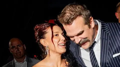 Getty Images Millie Bobby Brown and David Harbour close to each other in smart clothes on the red carpet