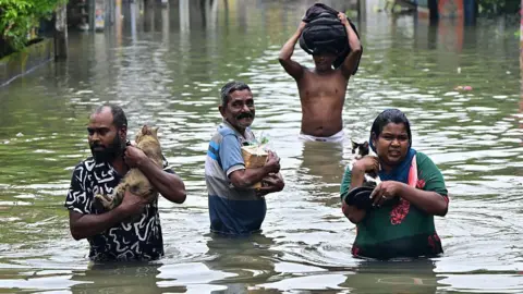 Getty Images People wade through a flooded road, a man and a woman holding cats in their arms, after heavy rainfall in Wellampitiya on the outskirts of Colombo, Sri Lanka
