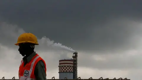 Getty Images A worker stands in front of a chemical factory as it discharges exhaust into the air of Mumbai, India, on Monday, Sept. 13, 2010.