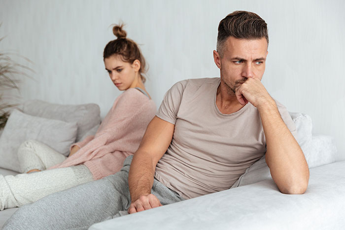 Man and woman sitting apart on couch looking upset, reflecting conflict over girlfriend's weight and past pounds.
