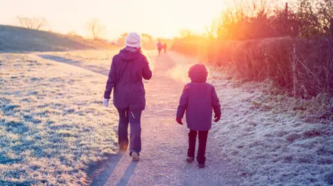 Getty Images A woman and young boy wearing winter wear walking on a path with frosted grass around them. 