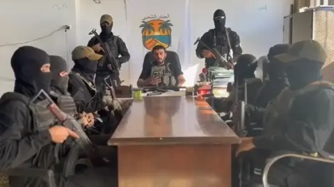 Ashraf al-Mansi Ashraf al-Mansi reads out a statement in front of armed men on 14 October 2025
