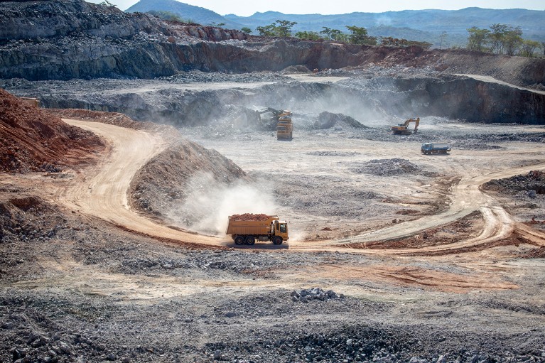 Industrial trucks hauling ore and rocks churn up dirt in an open pit lithium mine.
