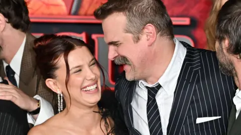 Getty Images Millie Bobby Brown and David Harbour standing closely and laughing together at the premiere