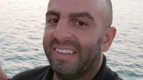 LNER Samir Zitouni is smiling at the camera in a close-up shot of his face. He is balding and has a moustache and a beard