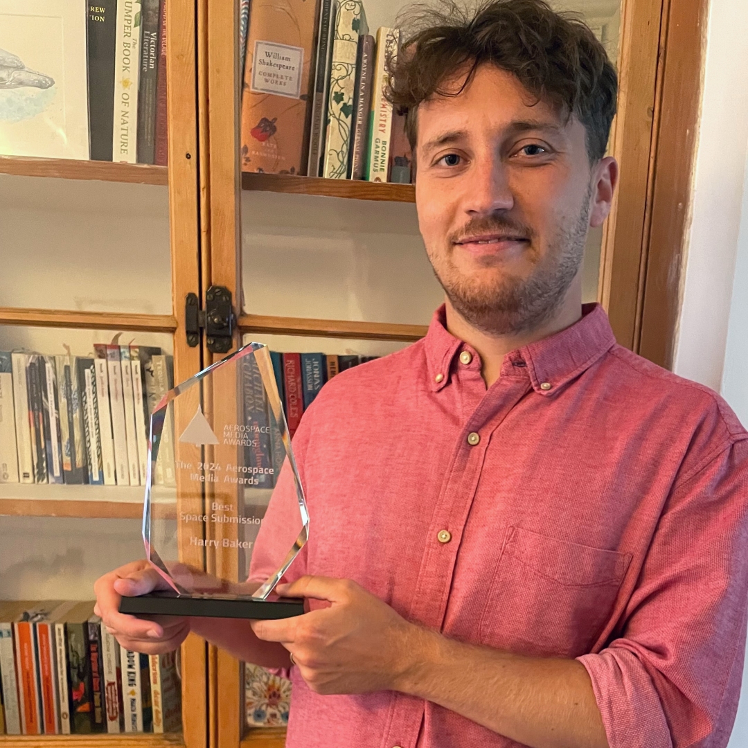 A man in a pink shirt holding a glass award in front of a bookcase