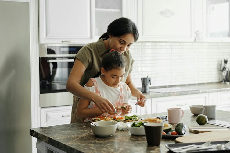 Mother and daughter cooking together in white kitchen.