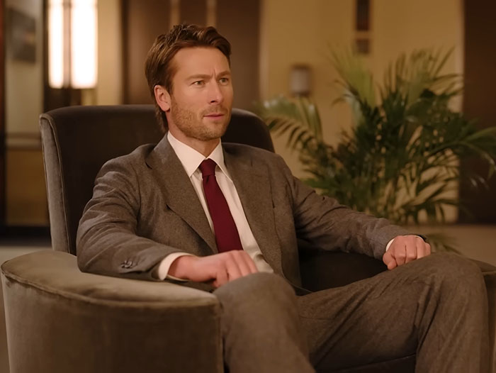 Glenn Powell seated in a suit, looking thoughtful, revealing emotional reason behind flying UPS driver to SNL. Glenn Powell seated in a suit, looking thoughtful, revealing emotional reason behind flying UPS driver to SNL.