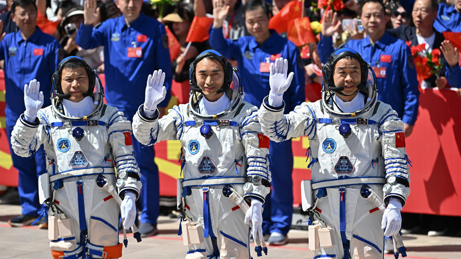 A photo of three Chinese astronauts waving to the cameras before launching to space