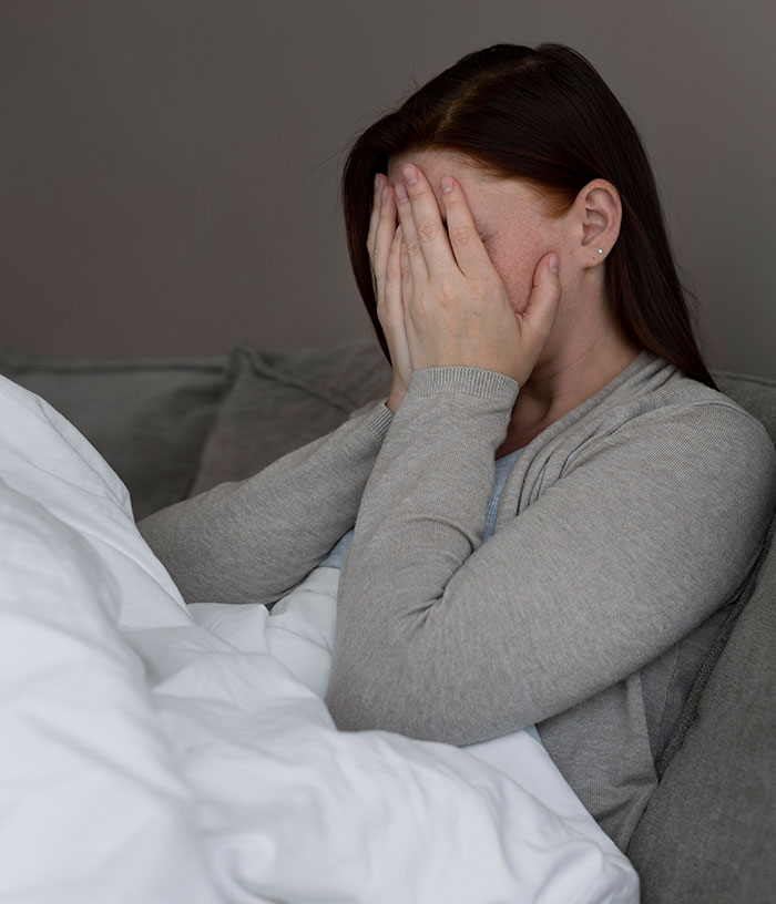 Woman sitting on couch with hands covering face, illustrating mysteries about the human body that science still hasn't explained.