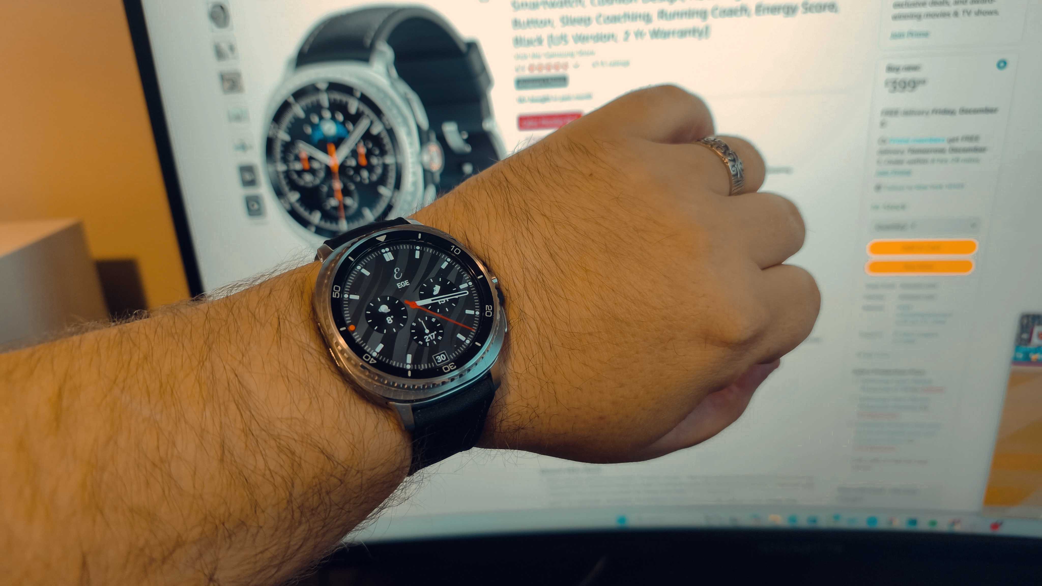 A hand wearing a Samsung Galaxy Watch 8 Classic in front of a monitor showing an Amazon deal on a Samsung Galaxy Watch 8 Classic