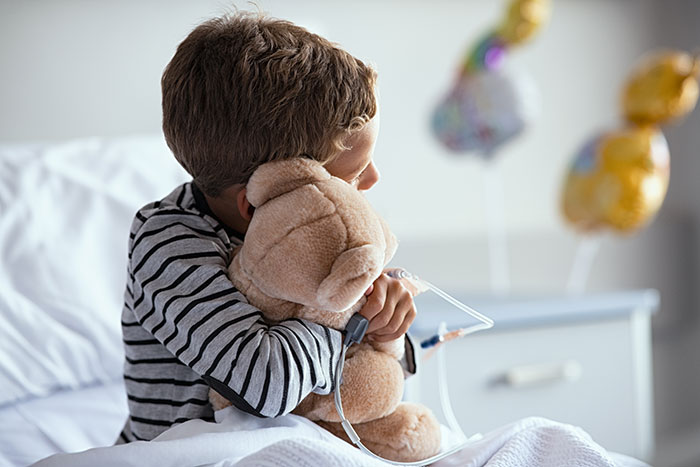 Young patient hugging a teddy bear in hospital bed, symbolizing strength and hope in coma survivor stories.