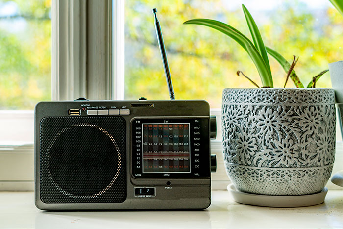 Portable black radio with antenna next to a gray decorative flower pot on a windowsill, coma survivors story concept.
