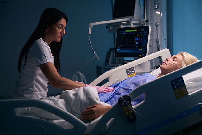 Nurse sitting beside a coma patient in a hospital bed, monitoring vital signs and providing care to a coma survivor.