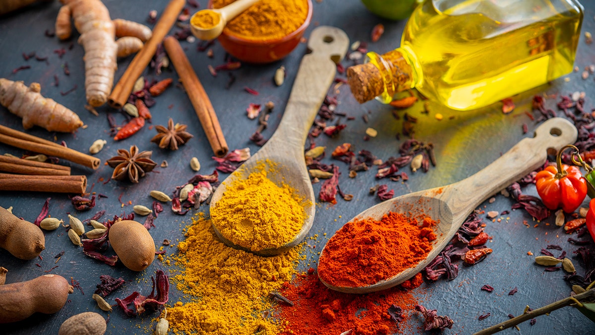 turmeric and saffron powder on two spoons on a table filled with spices and oil