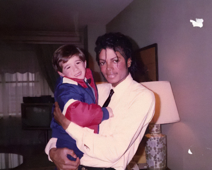 Michael Jackson holding a young child indoors, related to disturbing new sibling allegations amid biopic trailer release.