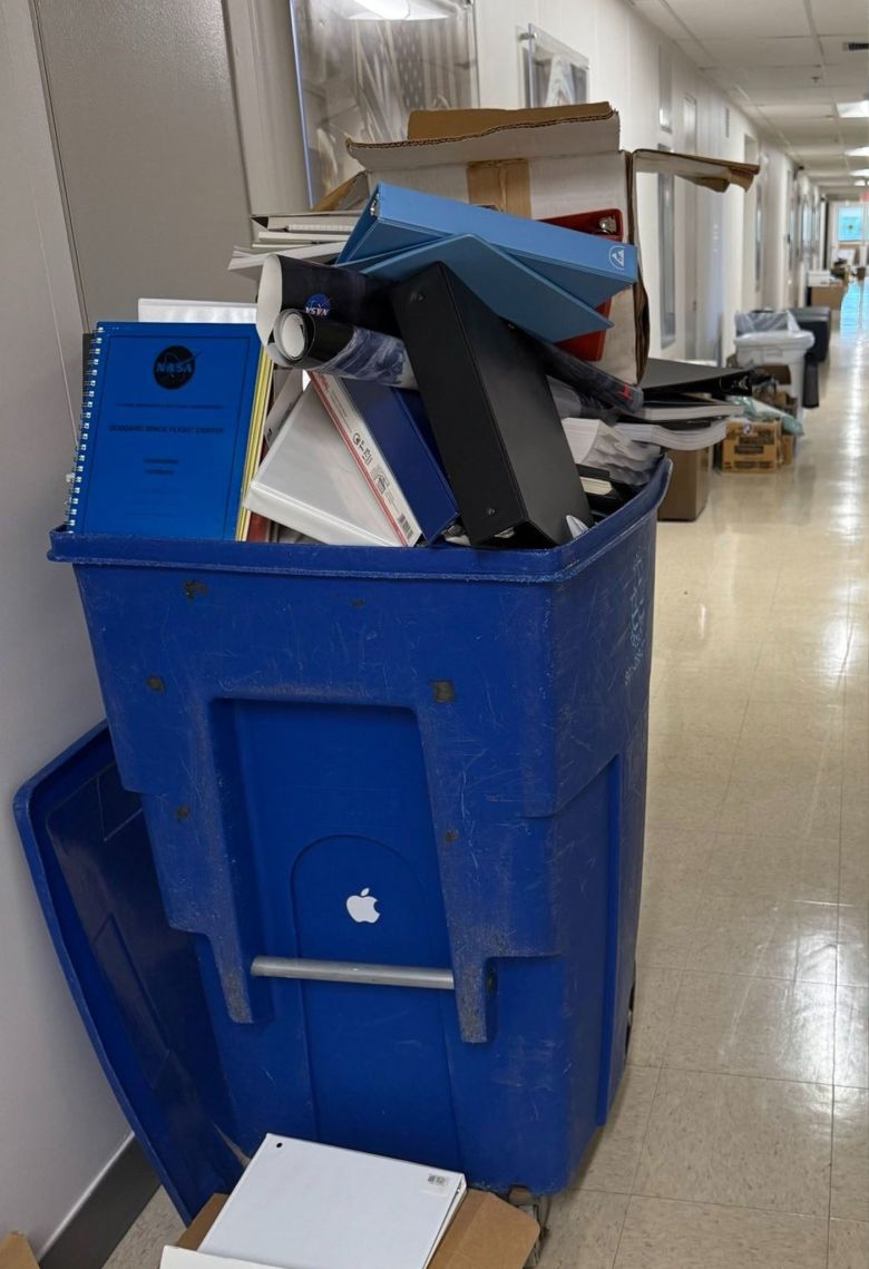 A blue trash bin is seen stuffed with discarded binders and paperwork.