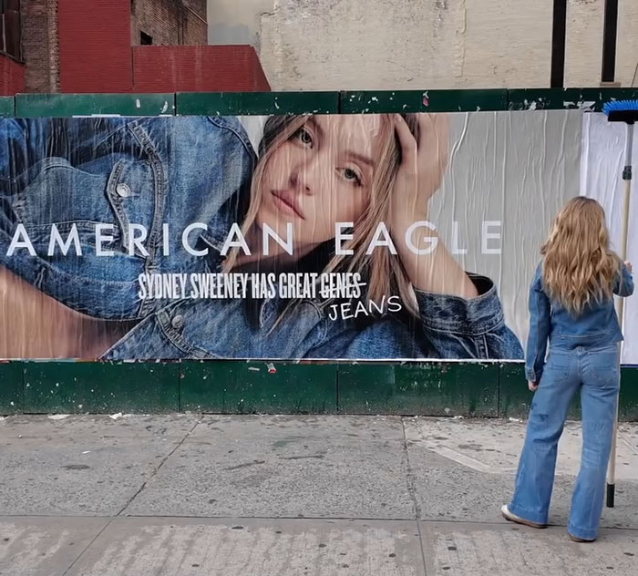 Sydney Sweeney standing in front of a large American Eagle jeans billboard in an urban setting.