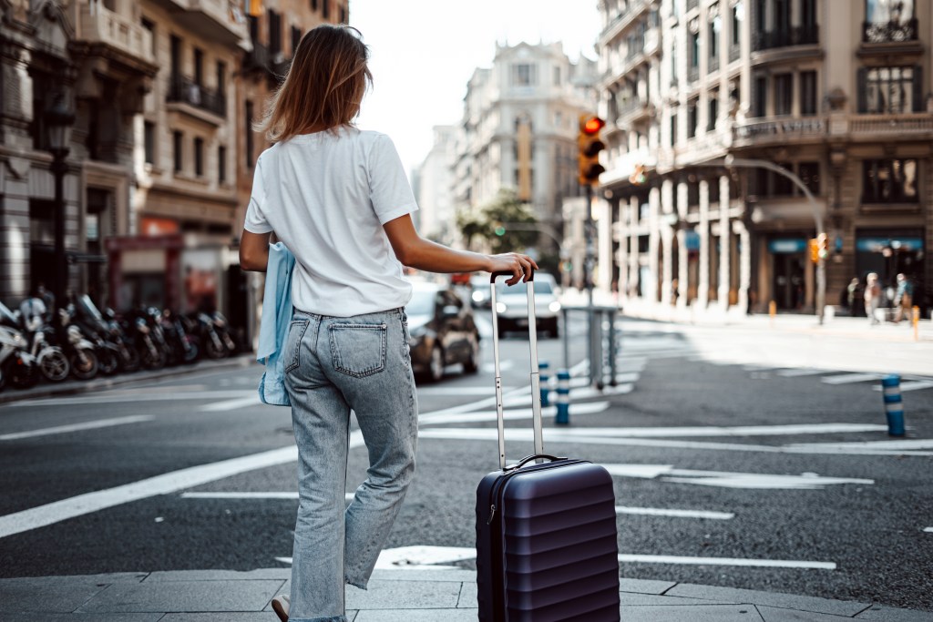 Traveling woman with a suitcase on a sunny city street.