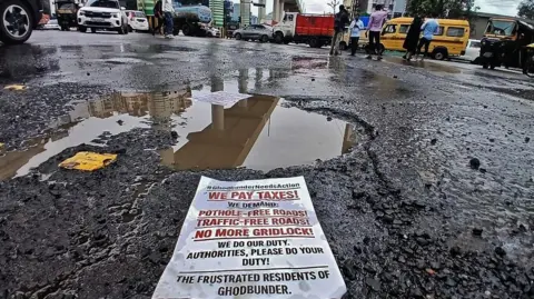 Hindustan Times via Getty Images A protest leaflet in front of a massive pothole in Thane - a satellite suburb of Mumbai. 