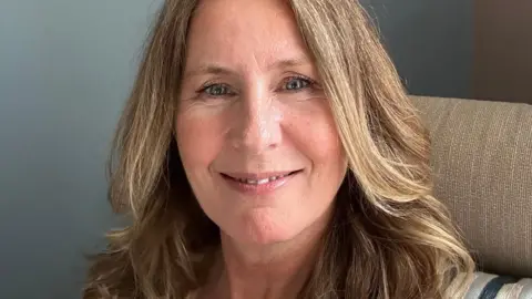 Traci smiles at the camera while sitting in a chair, in a close-up shot.