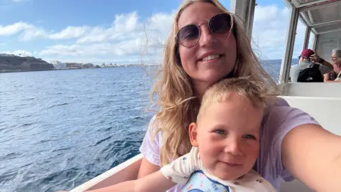 Contributed Megan has long blonde wavy hair and is taking a selfie of herself and Edward, who is sitting on her lap. They are on a boat in the sunshine, with white hotels in the background along the coastline.