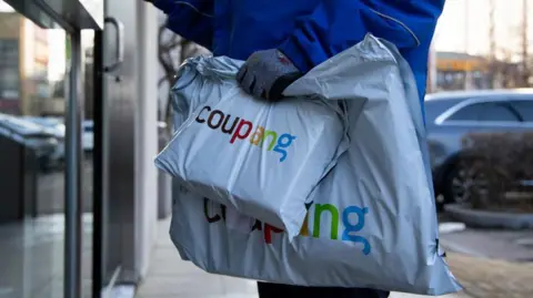 Getty Images A Coupang employee holds packages in front of an apartment building in Bucheon, South Korea
