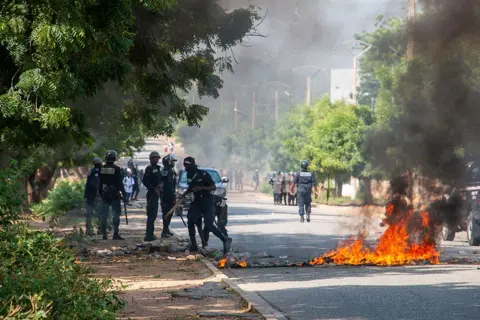 AFP via Getty Images Members of the Cameroonian police are seen near a burning barricade that is burning in the middle of a road in Garoua, northern Cameroon.