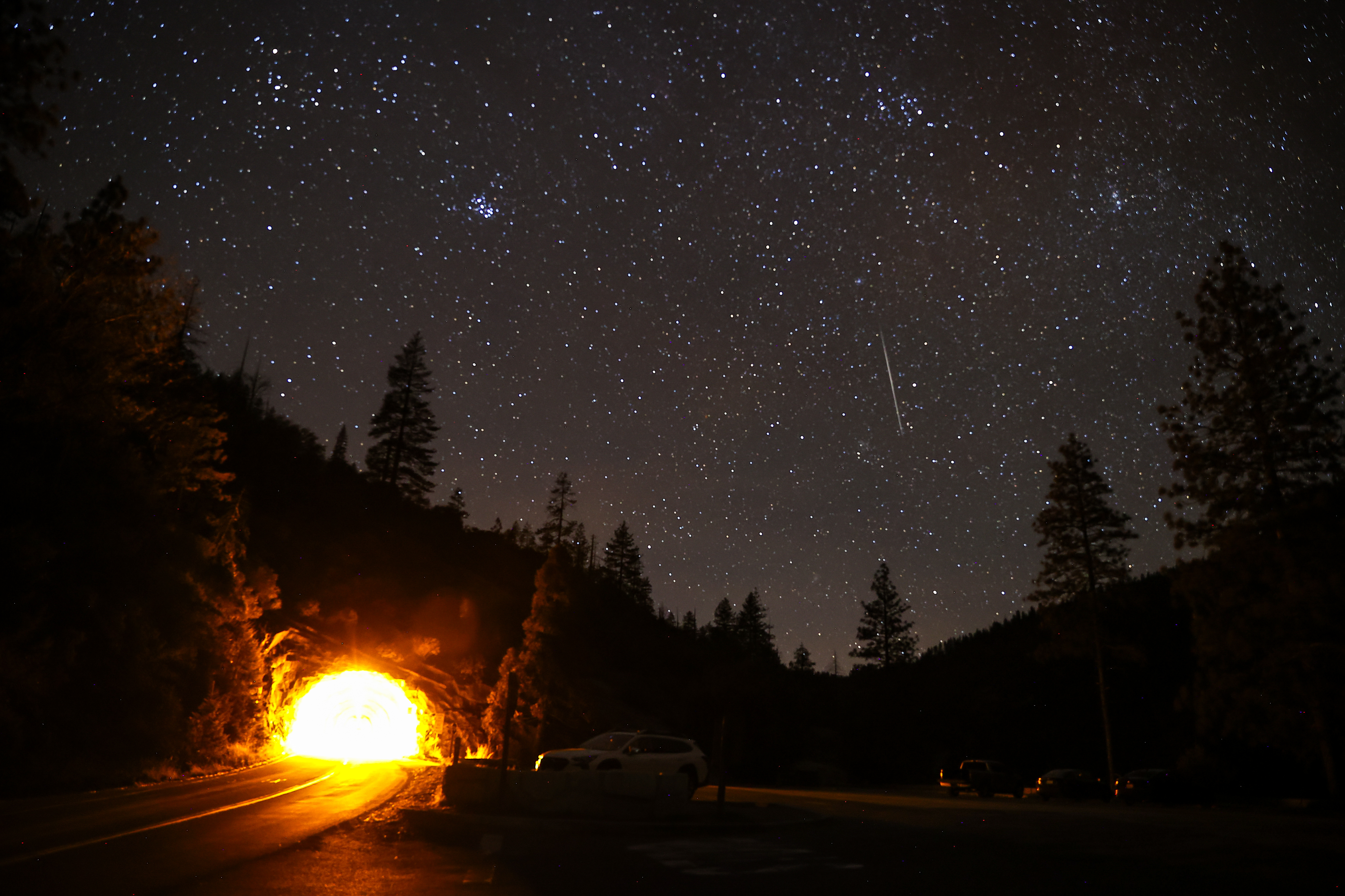 A photo of the Geminid meteor shower above stargazers gathering in a carpark at Valley View in Yosemite National Park.