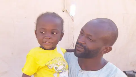 Ed Habershon / BBC Abdullah Adam Mohamed, holding one of his young daughters who is wearing a yellow T-shirt