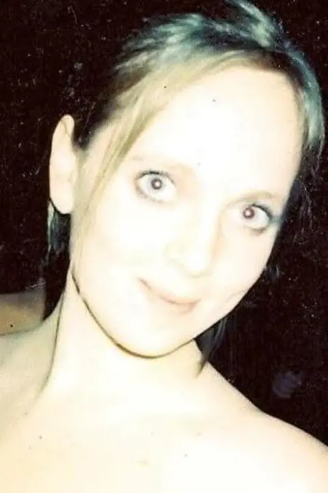 Jenny Evans Jenny Evans smiles at the camera, she is wearing a red top and has her hair up in an up do. It is a head and shoulders shot of her.