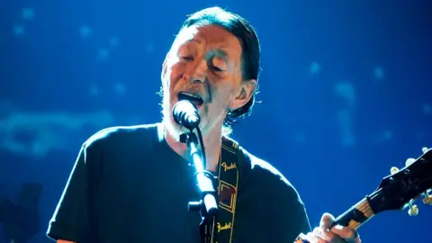 Getty Images Chris Rea singing on stage and playing the guitar in 2017