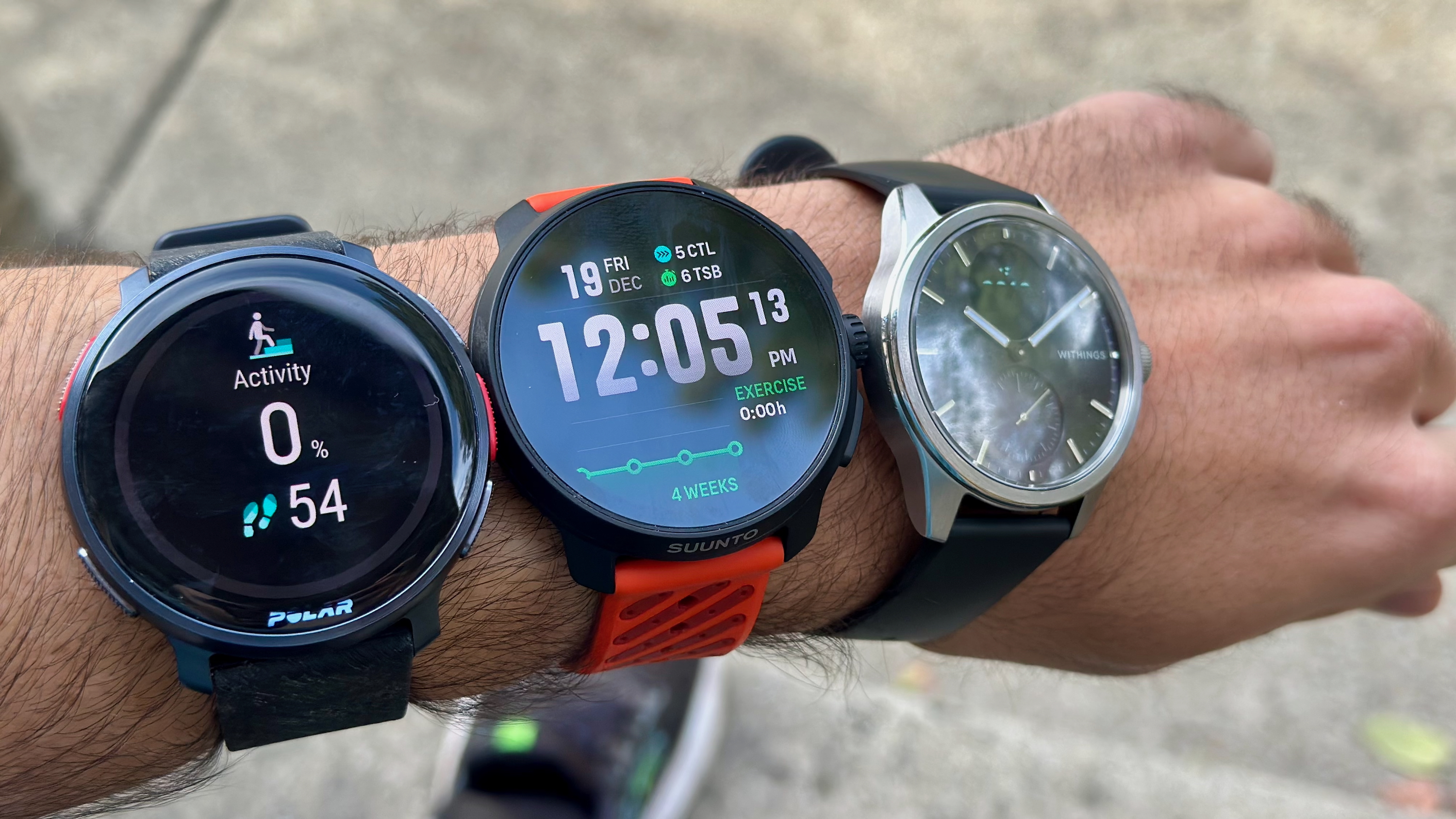 A photo of the Polar Vantage V3, Suunto Race 2, and Withings ScanWatch 2 all strapped onto one arm.