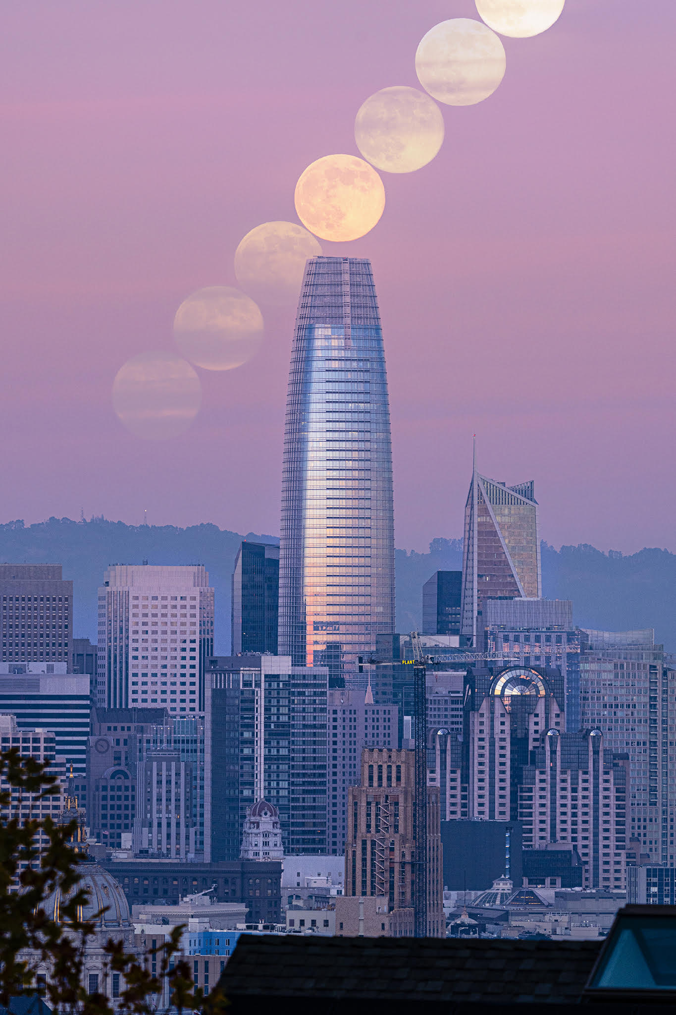 A series of full moons form a diagonal line in the pink evening sky over a modern city with a central skyscraper dominating the middle of the image.