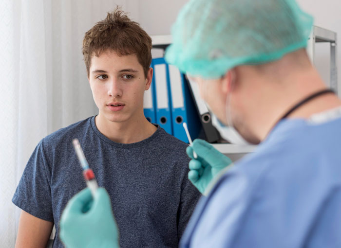 Teen boy in a medical exam room looking at doctor preparing a syringe, representing diabetes and weight health concerns. Teen boy in a medical exam room looking at doctor preparing a syringe, representing diabetes and weight health concerns.