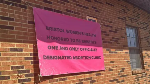 A pink sign hung on a brick building reads: Bristol Women's Health is honored to be Bristol's one and only officially designated abortion clinic