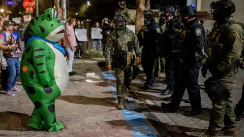 Getty Images A man in a frog suit faces off with a group of law enforcement in Portland