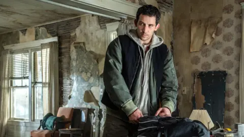 Universal Josh O'Connor standing in a grand but fading room, opening a bag