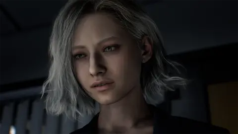 Capcom Screenshot shows a young woman with chin length, whiteish hair in a darkened room. Her face is illuminated by the glow from a screen, which can be seen reflected in her eyes. She looks concerned as she views what's in front of her.