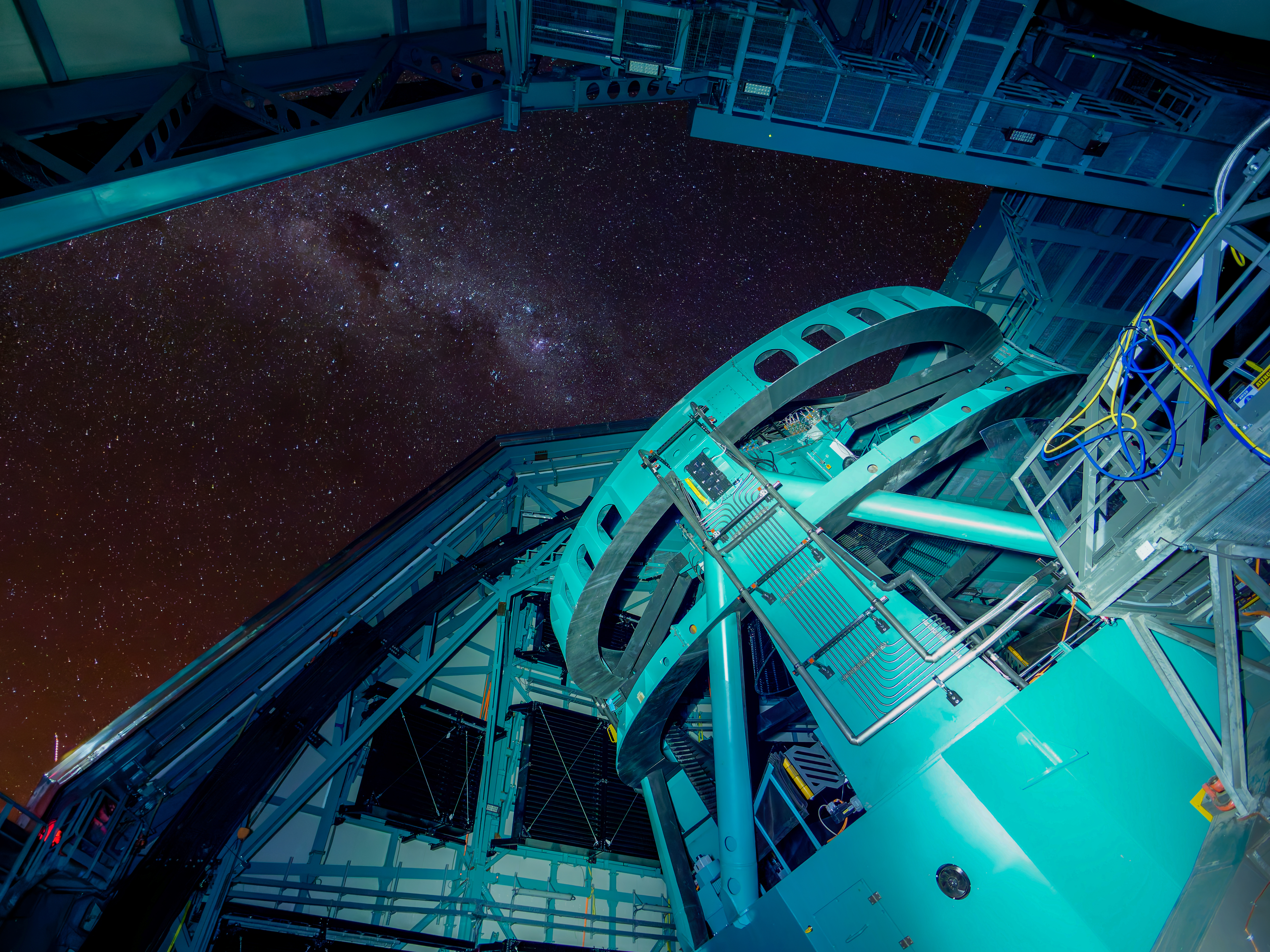 A view of a large telescope system within the Rubin Observatory with a starry night scene above the open roof