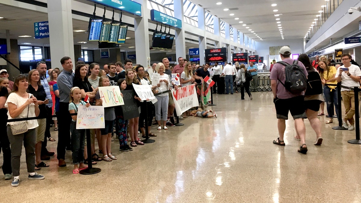groups of people waiting at airport with signs to greet loved ones.