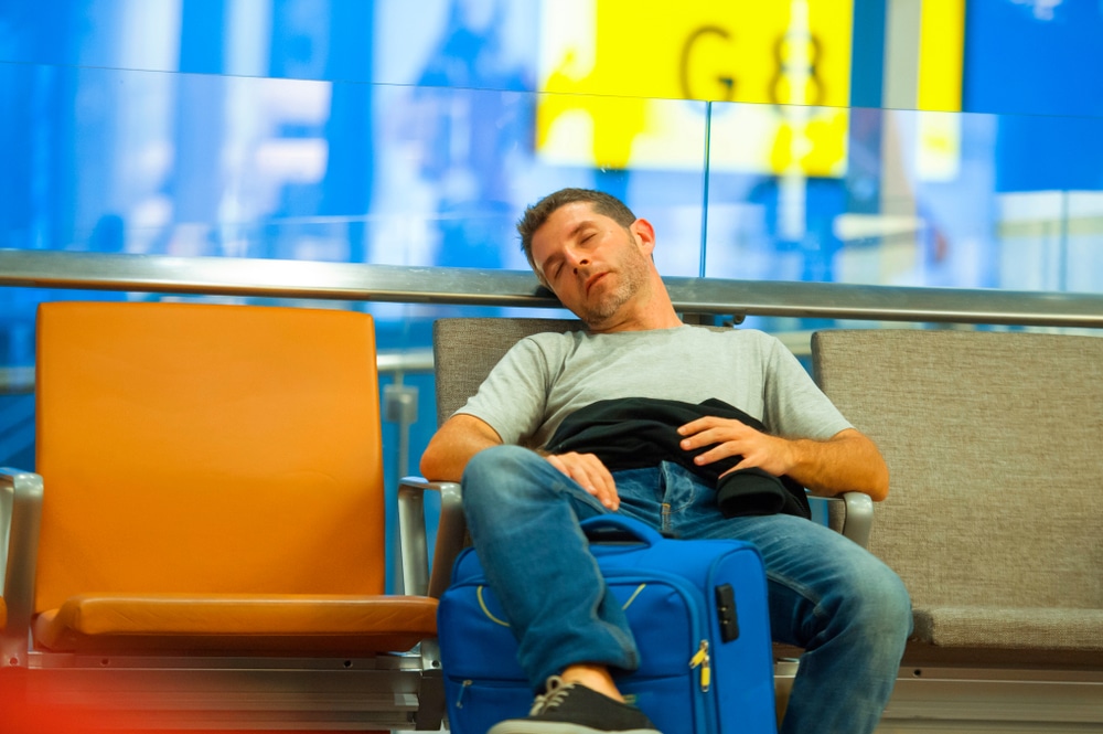 Tourist With A Suitcase Sleeping At Boarding Gate Waiting For His Delayed Flight