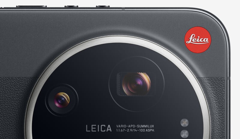 Close-up of a camera lens module labeled "Leica" with two visible lenses and a red Leica logo on the top right corner against a gray background.