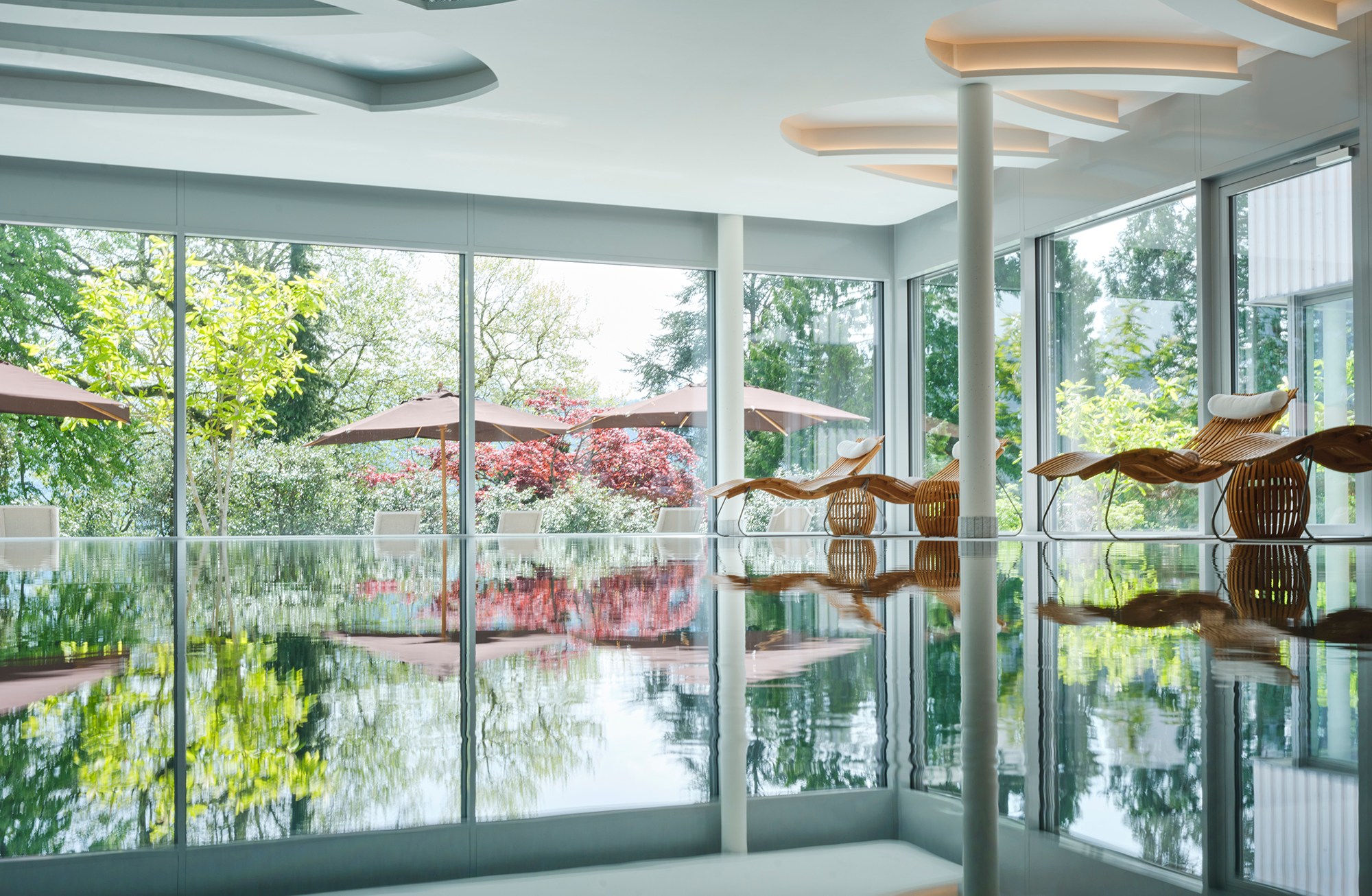 Indoor pool area with lounge chairs and large windows overlooking lush trees.