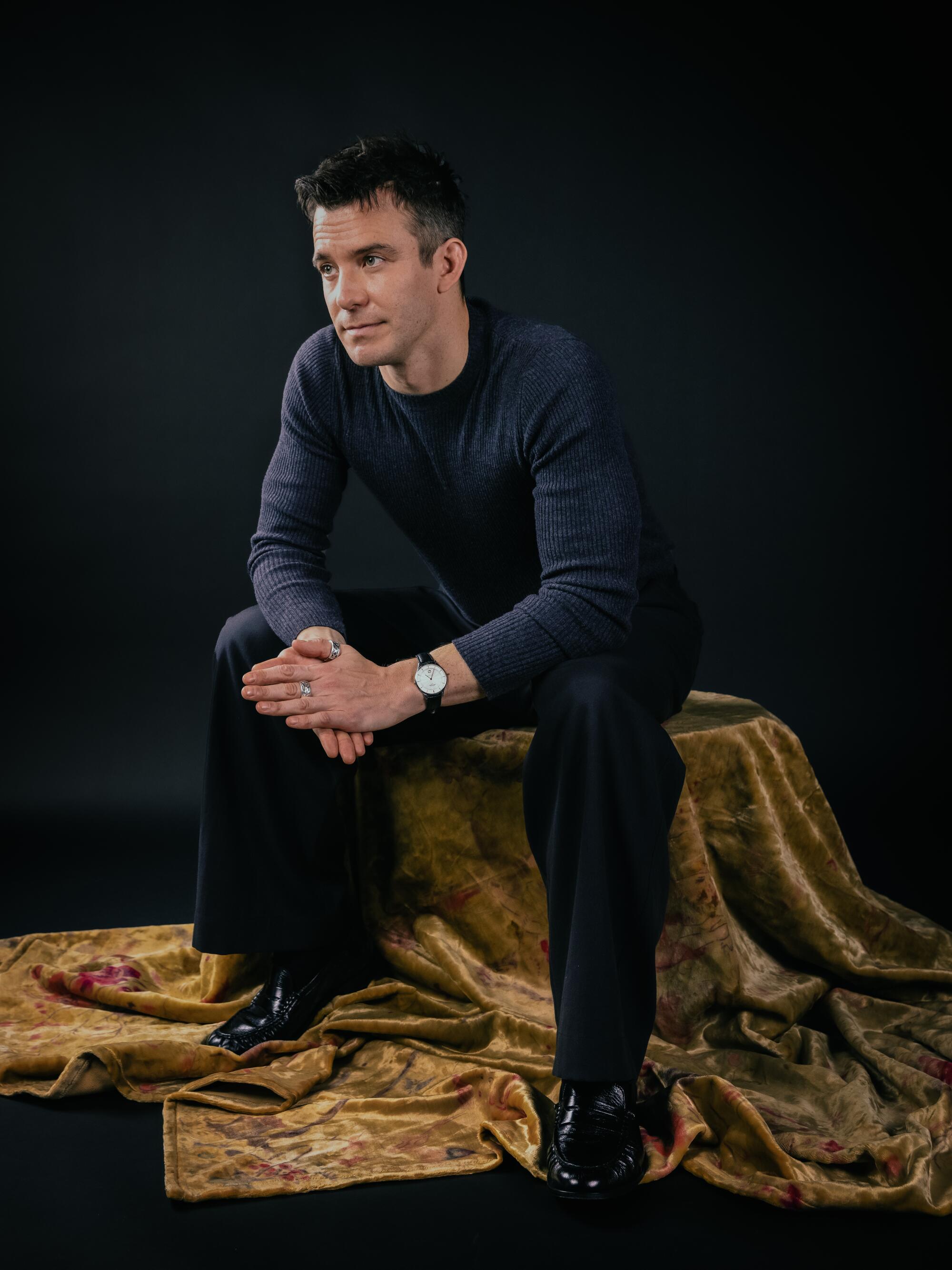 A man poses for a photo on a stool draped with fabric