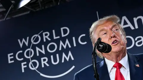 AFP via Getty Images Close up shot of Donald Trump speaking into a microphone in front of a board with the words "World Economic Forum" on it.