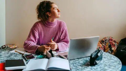 Getty Images Woman reflecting by looking out of a window while sitting at her laptop