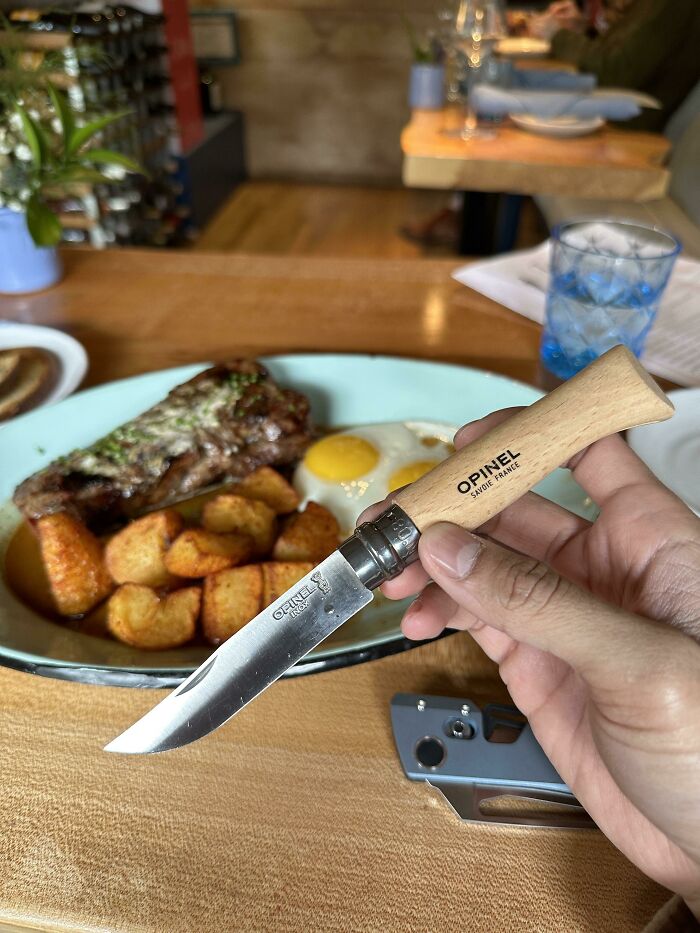 Hand holding an Opinel knife over a plate with steak, fried potatoes, and a fried egg, related to mysteries people would love to solve.