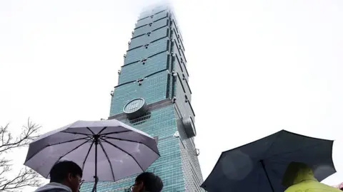 Getty Images People stand under umbrellas at the bottom of Taipei 101 in Taiwan 