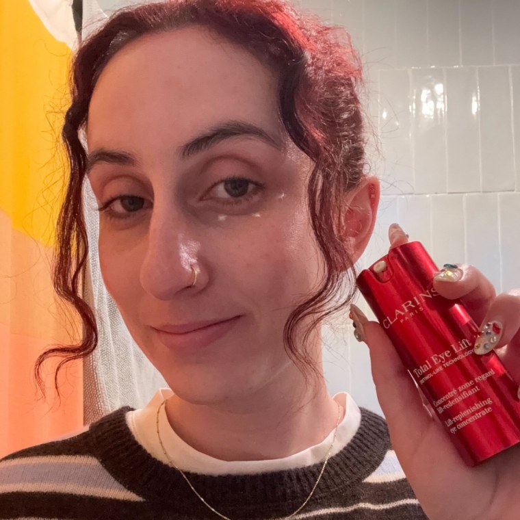 Woman wearing an eye cream while showing packaging